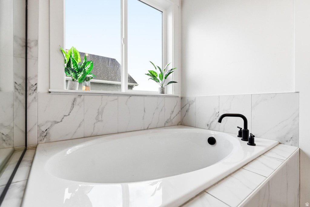 Built-in soaking tub featuring a matte black faucet, surrounded by white tile with grey veining, and a window providing natural light