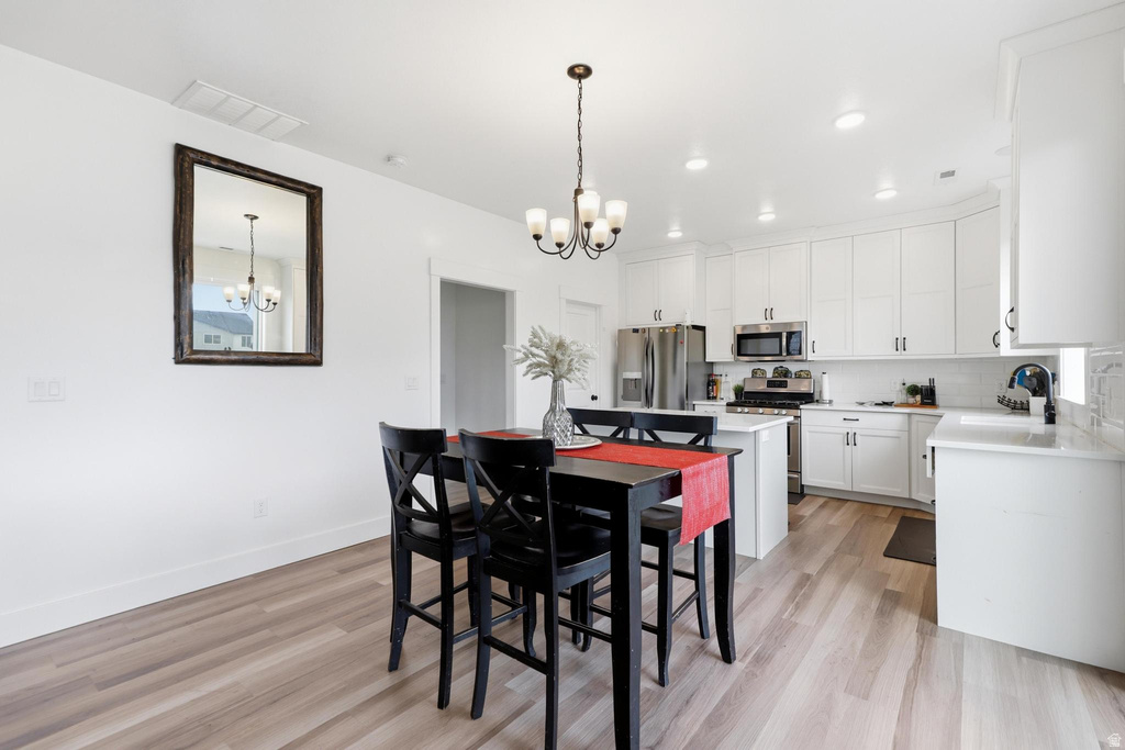 Bright kitchen featuring white cabinetry, light countertops, wood-finish flooring, a contemporary chandelier, and stainless steel appliances