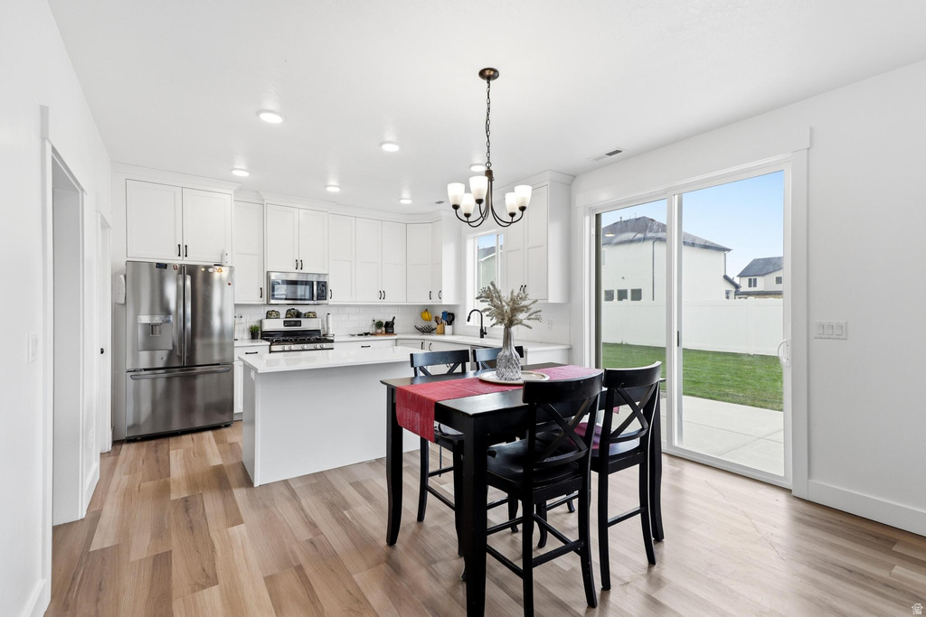 Kitchen and dining area featuring wood-finish flooring, white cabinetry, stainless steel appliances, a center island with a white countertop, and a sliding glass door to the backyard patio