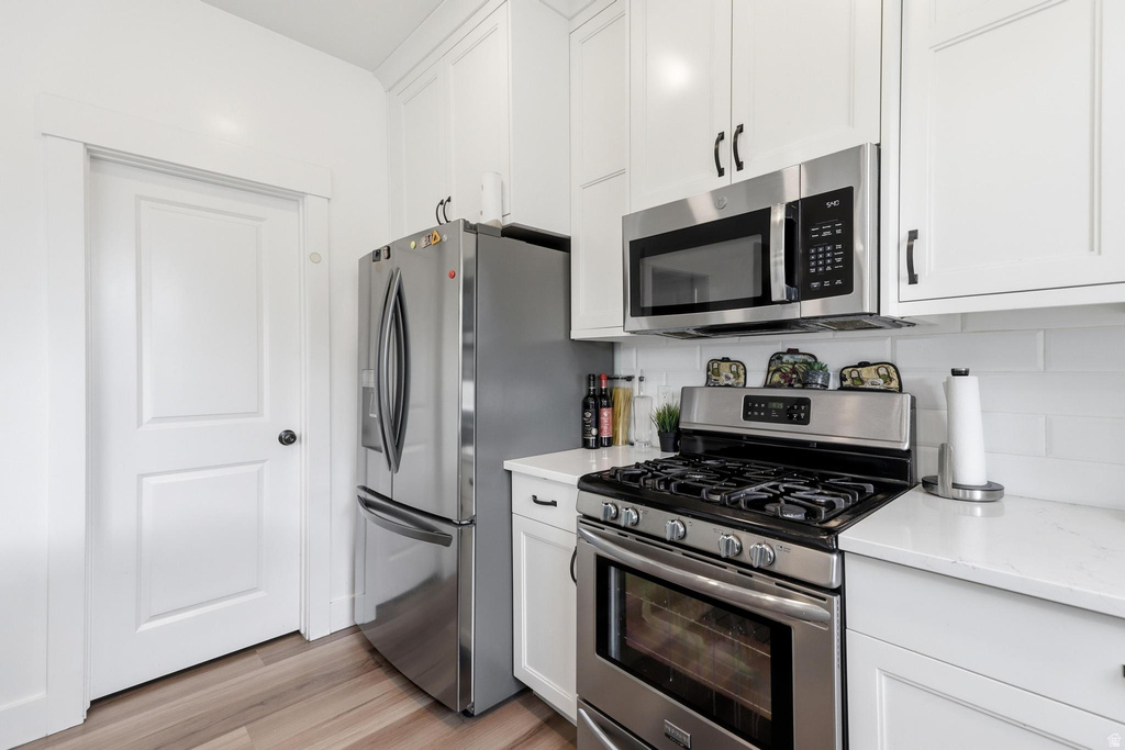 Kitchen featuring stainless steel appliances, white subway tile backsplash, white shaker cabinetry with black hardware, white countertops, and wood-finish flooring