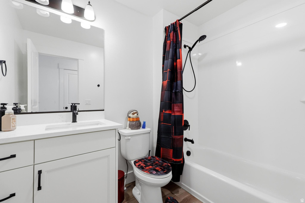 Full bathroom featuring a white vanity with integrated sink, matte black fixtures, a contemporary vanity light, a bathtub with a shower, and wood-finish flooring