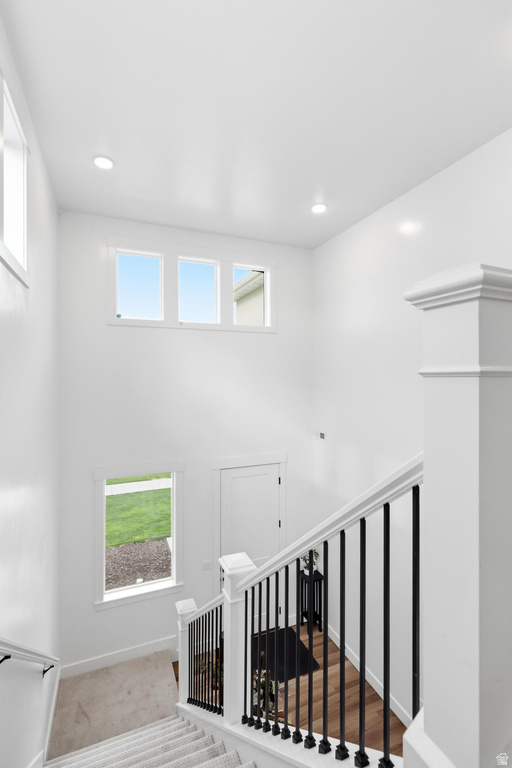 Two-story foyer featuring a contemporary staircase with black wrought iron spindles and white newel posts, high ceilings, recessed lighting, and multiple windows