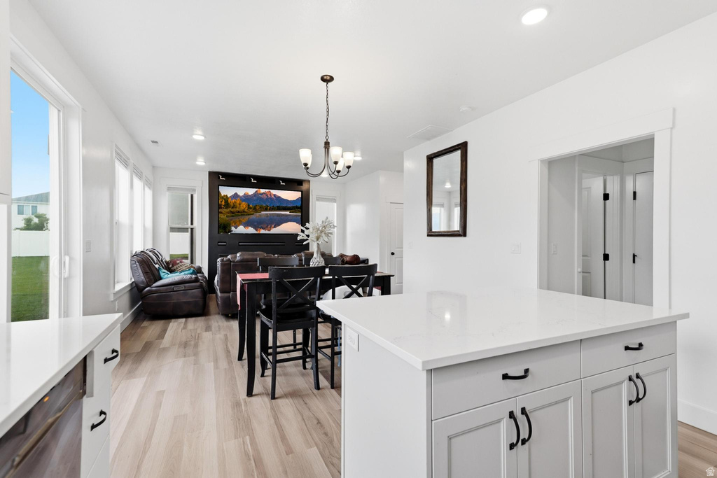Spacious open-concept living area featuring a kitchen island with white countertop, recessed lighting, wood-finish flooring, ample natural light from multiple windows, and a built-in media center