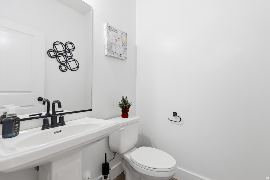 Pedestal sink with a matte black faucet, wall-mounted mirror, and white toilet