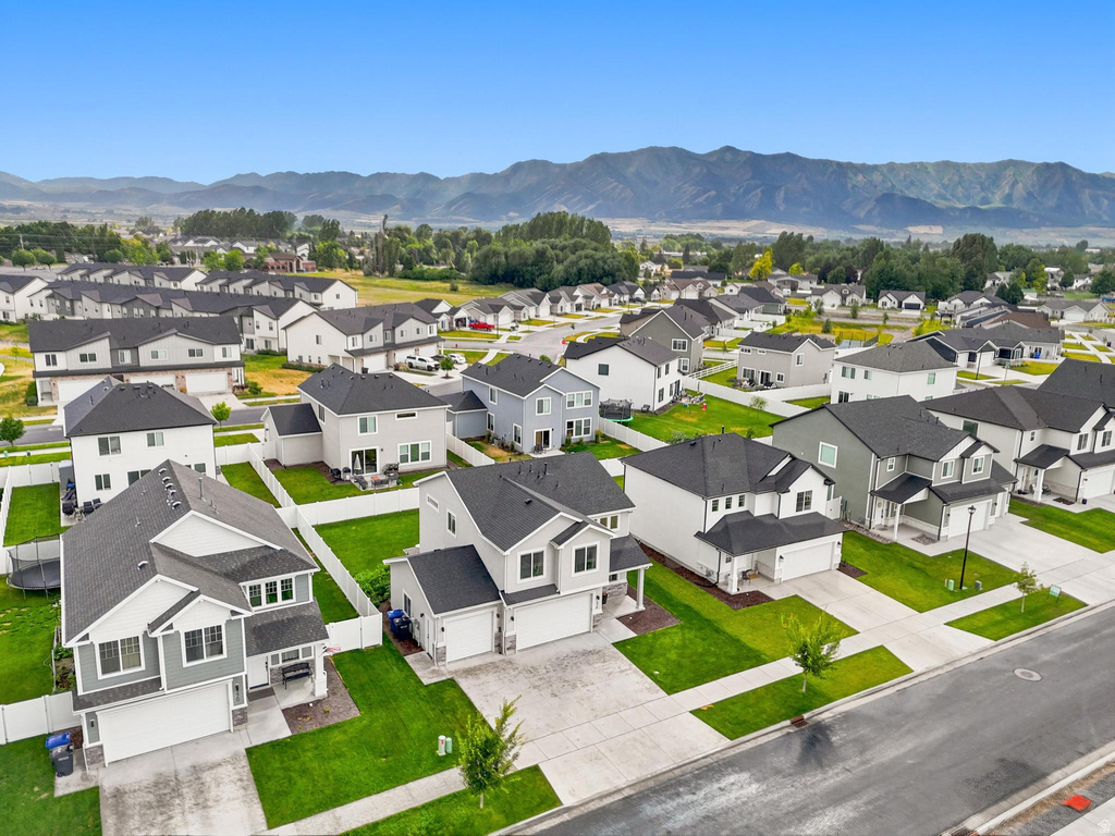 Residential neighborhood featuring contemporary two-story homes with attached garages, manicured lawns, and white perimeter fencing, set against a mountain backdrop