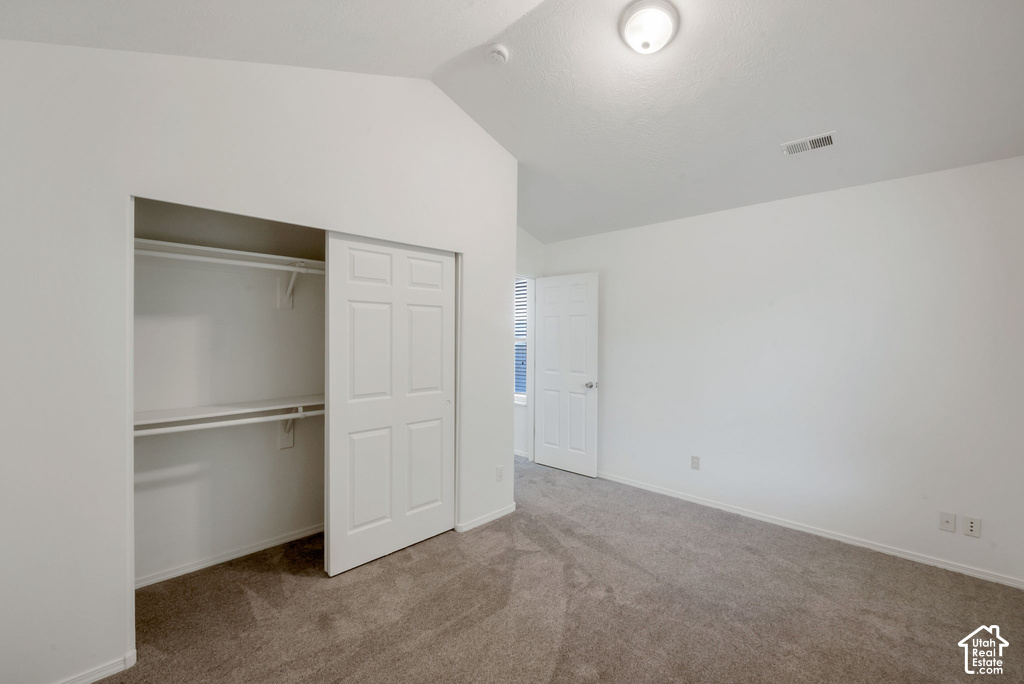 Bedroom featuring vaulted ceilings, plush carpet flooring, a bifold closet with shelving and hanging rods, and a white paneled door