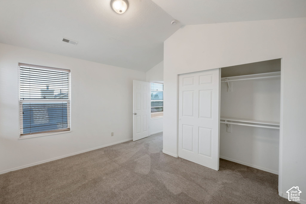 Carpeted room featuring a vaulted ceiling and a window with blinds