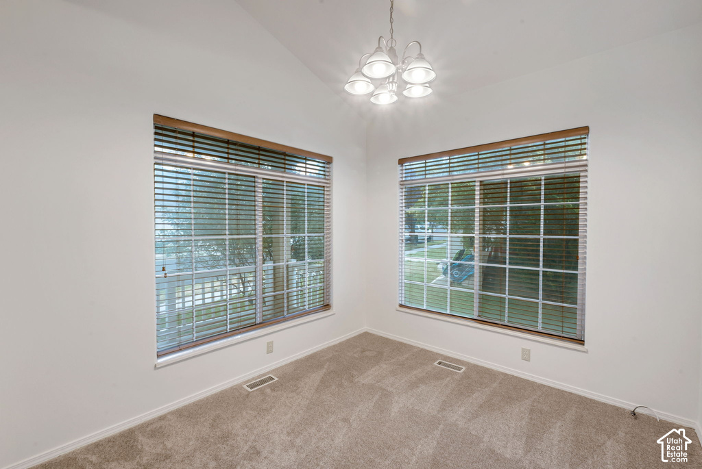 Vaulted ceiling room featuring two large windows with horizontal blinds and wood-finish trim, a five-light chandelier, and carpeted flooring