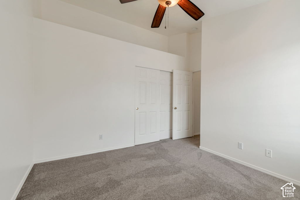 Spacious room featuring neutral carpet flooring, white walls, a ceiling fan with integrated lighting, and a closet with bifold doors