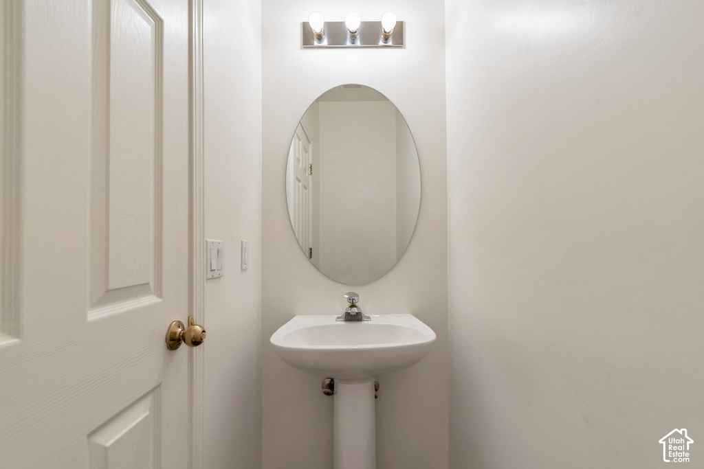 Pedestal sink with a polished chrome faucet, an oval mirror, and a three-light vanity fixture