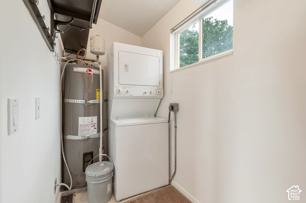 Dedicated laundry area featuring a stacked washer and dryer, water heater, and an upper window providing natural light