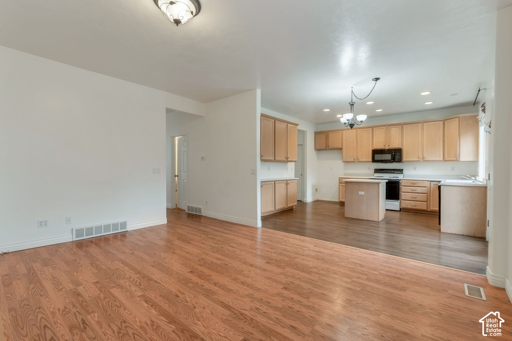 Open-concept living area featuring wood-finish flooring and a kitchen with light wood cabinetry, a central island, and black appliances