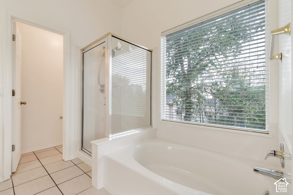 Bathroom featuring a built-in bathtub with a window, a glass-enclosed shower, and tile flooring