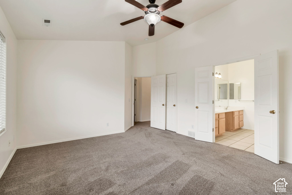 Spacious carpeted room featuring a vaulted ceiling with a ceiling fan, a window with horizontal blinds, and double doors opening to a bathroom with dual vanities