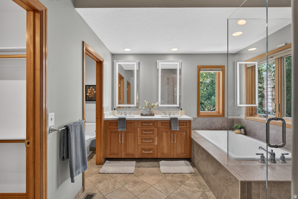 Bathroom featuring a dual vanity with a light-toned countertop, a built-in tub with tile surround, a glass-enclosed shower, and wood-framed windows