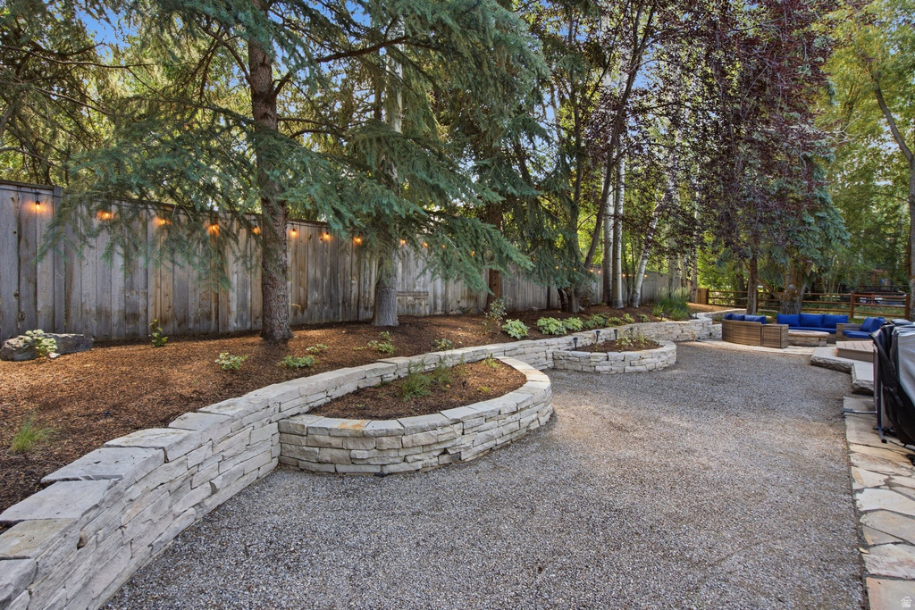 Landscaped backyard featuring layered stone retaining walls, a gravel patio area, mature trees, and a privacy fence with string lighting