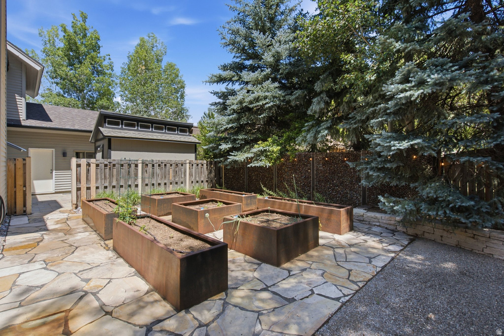 Outdoor flagstone patio featuring multiple rectangular planters, surrounded by mature trees, a privacy fence, and an exterior building with horizontal siding