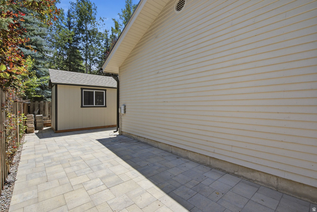 Side yard featuring a paver patio, a detached storage shed with a shingle roof and double-pane window, and horizontal siding on the main structure