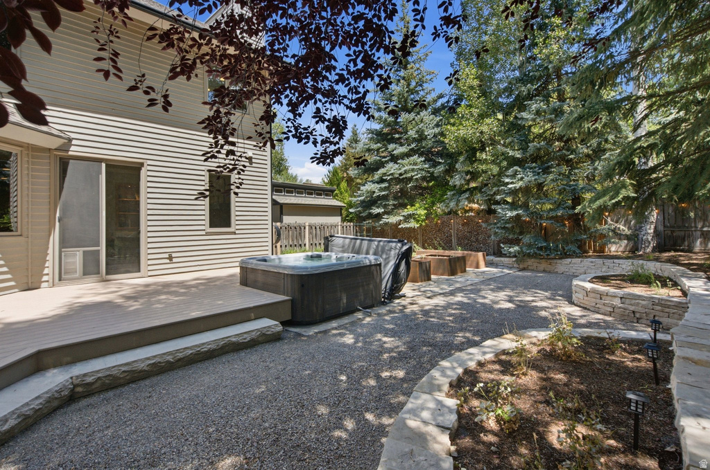 Backyard deck featuring a hot tub, gravel patio, stone retaining walls, and mature evergreen trees