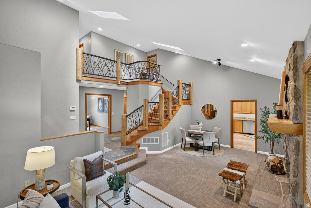 Multi-level interior featuring a stone-clad fireplace with a wood mantel, a natural wood staircase with decorative metal railings, and a vaulted ceiling with recessed lighting