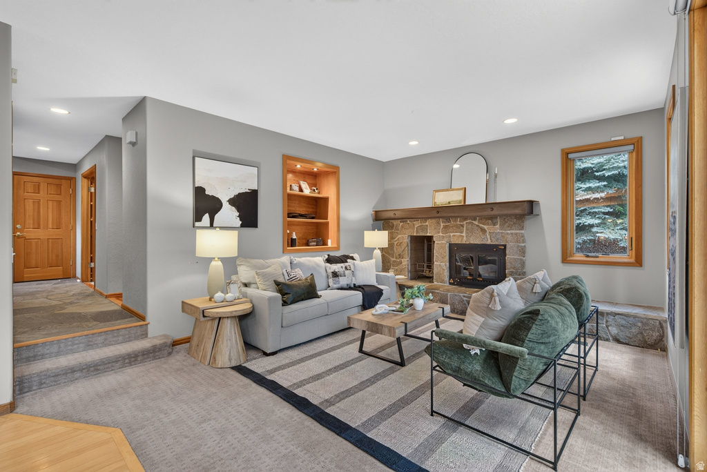 Living area featuring a stone fireplace with a substantial wood mantel, recessed lighting, a built-in wood shelving unit, and a wood-trimmed window