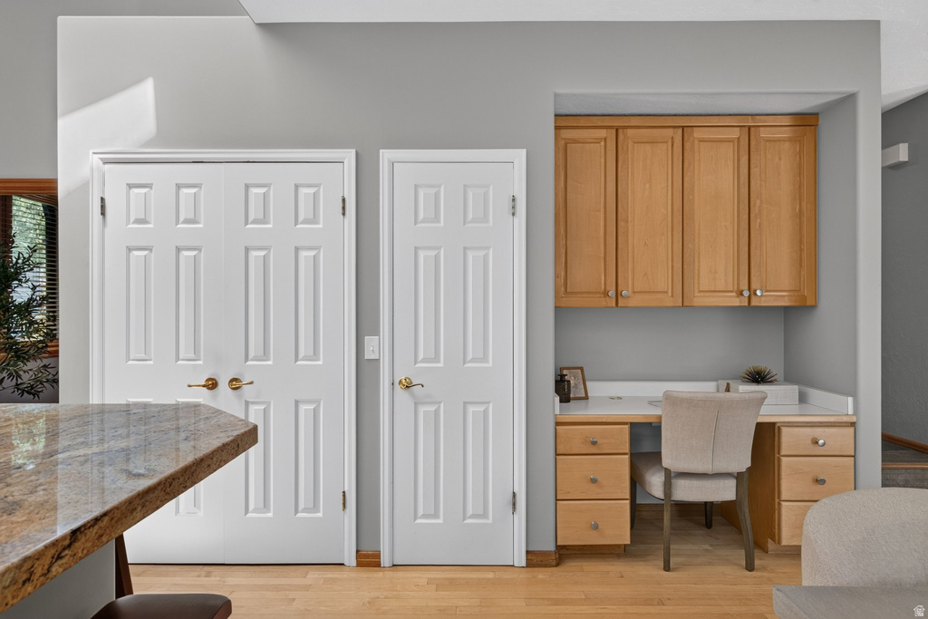 Integrated built-in desk with natural wood cabinetry and a light-toned countertop, complemented by two panel doors and wood-finish flooring
