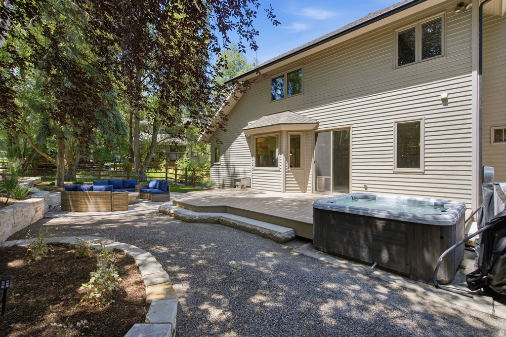Rear exterior featuring a spacious composite deck, built-in spa, sliding glass door, bay window, and gravel patio area with stone retaining walls