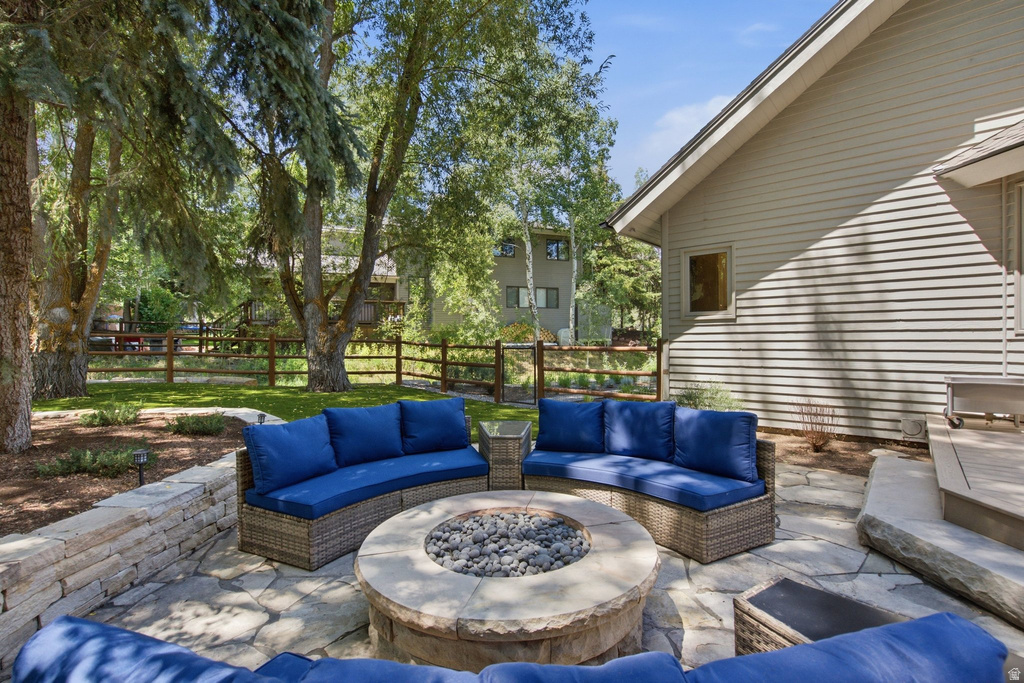 Stone patio featuring a built-in fire pit, stone retaining wall, and mature landscaping