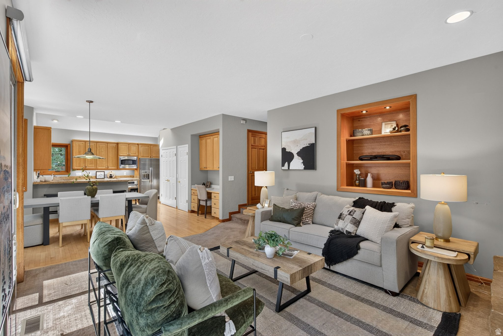 Open-concept living space with light wood-finish flooring, a built-in recessed wooden shelving unit, and recessed lighting