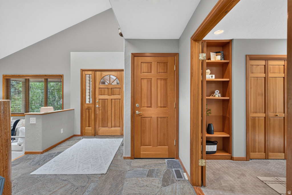 Entryway featuring slate tile flooring, a wood-finish front door with arched glass, a side window with horizontal blinds, and a built-in wood-finish shelving unit