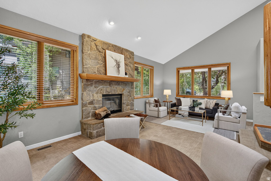 Living area featuring a stone fireplace with a wood mantel, vaulted ceilings, and natural wood-framed windows