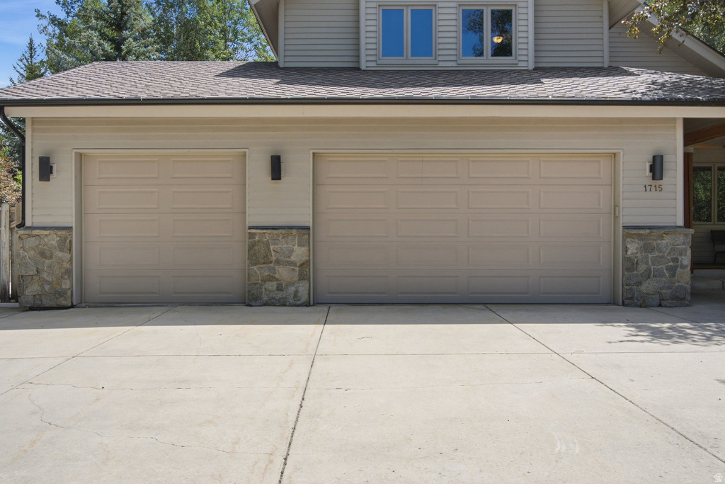 Two-car garage with panel doors, stone detailing, exterior sconces, and a concrete driveway
