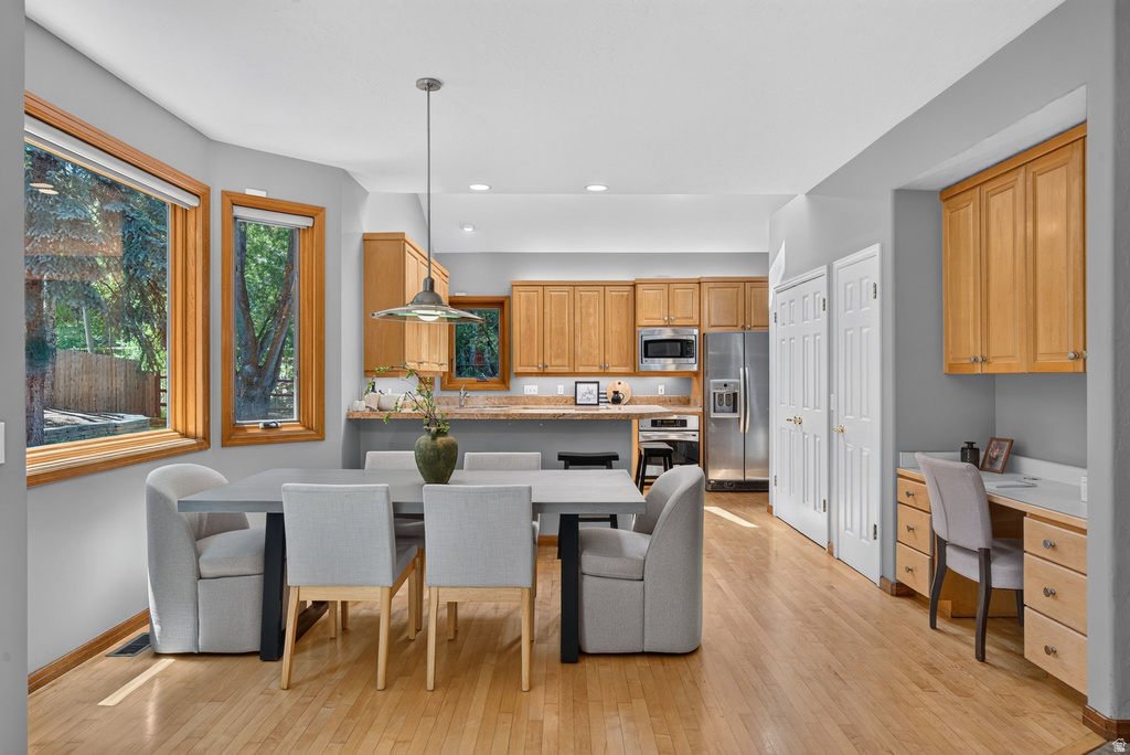 Kitchen and dining area featuring wood-finish flooring, light wood cabinetry, stainless steel appliances, and a built-in desk area