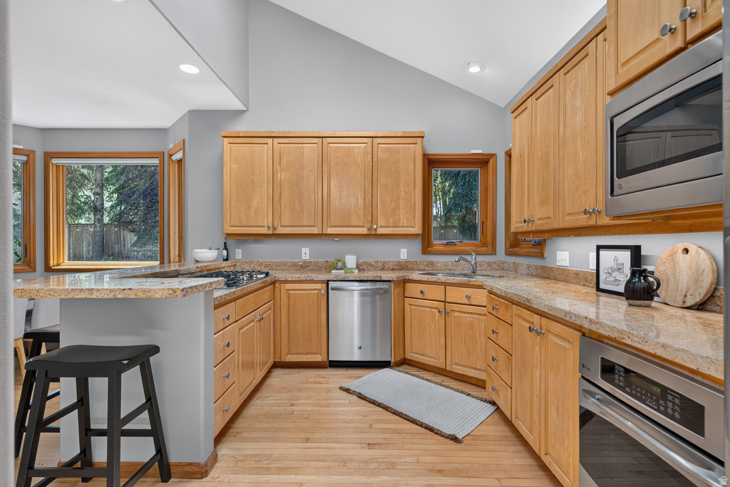 Kitchen featuring natural wood cabinetry, light-toned countertops, stainless steel appliances, and wood-finish flooring