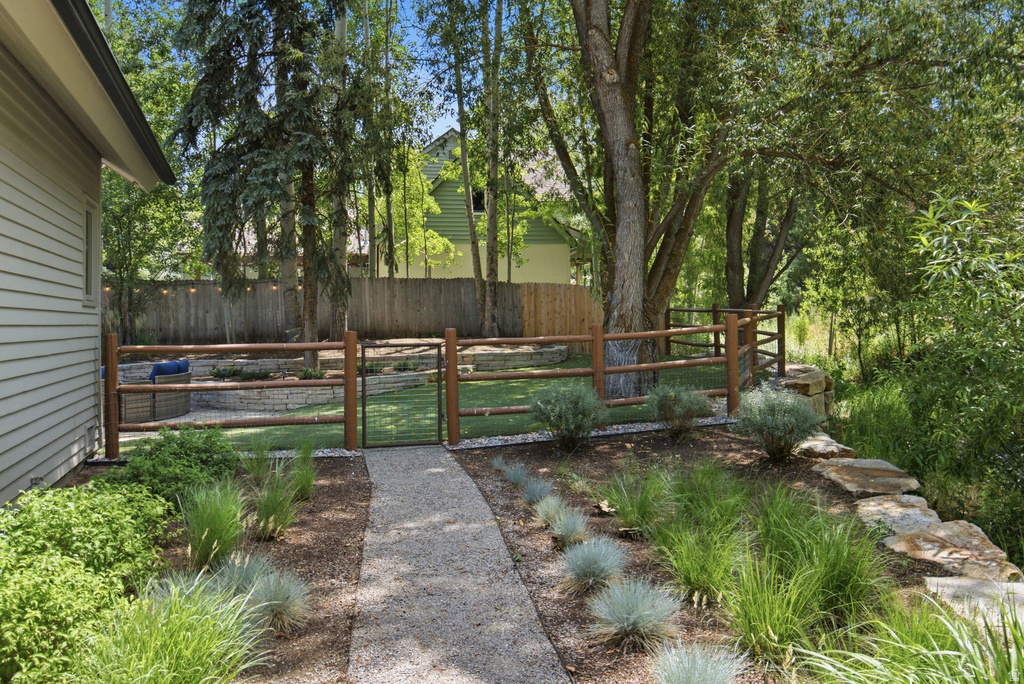 Landscaped backyard featuring a gravel pathway, a split-rail fence with a metal gate, mature trees, and a stone retaining wall