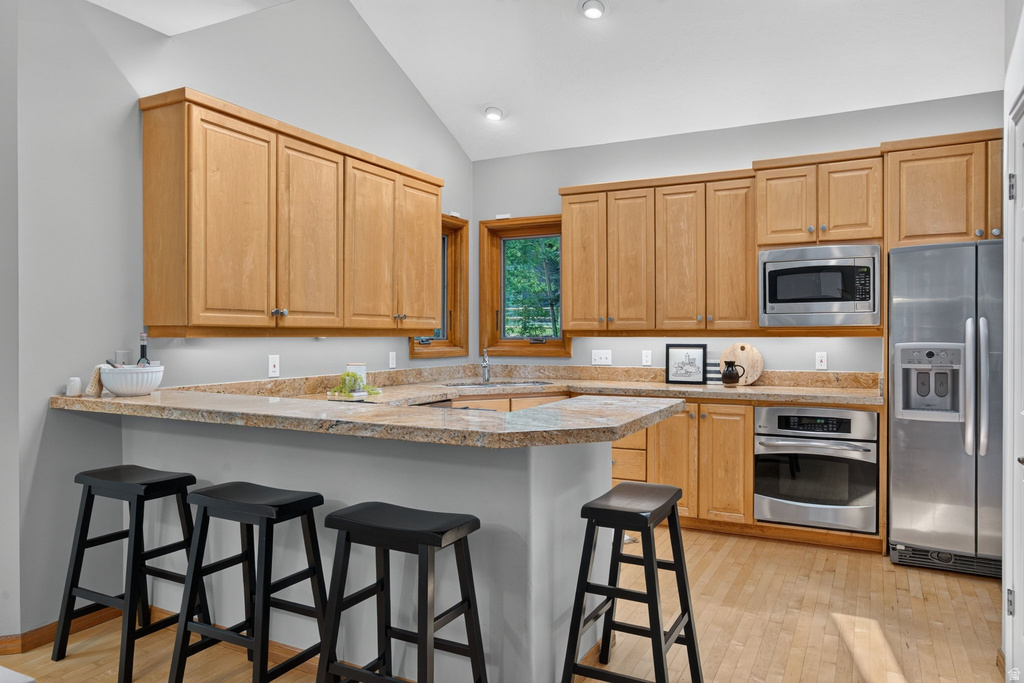 Kitchen featuring light wood cabinetry, stone countertops, stainless steel appliances, and wood-finish flooring