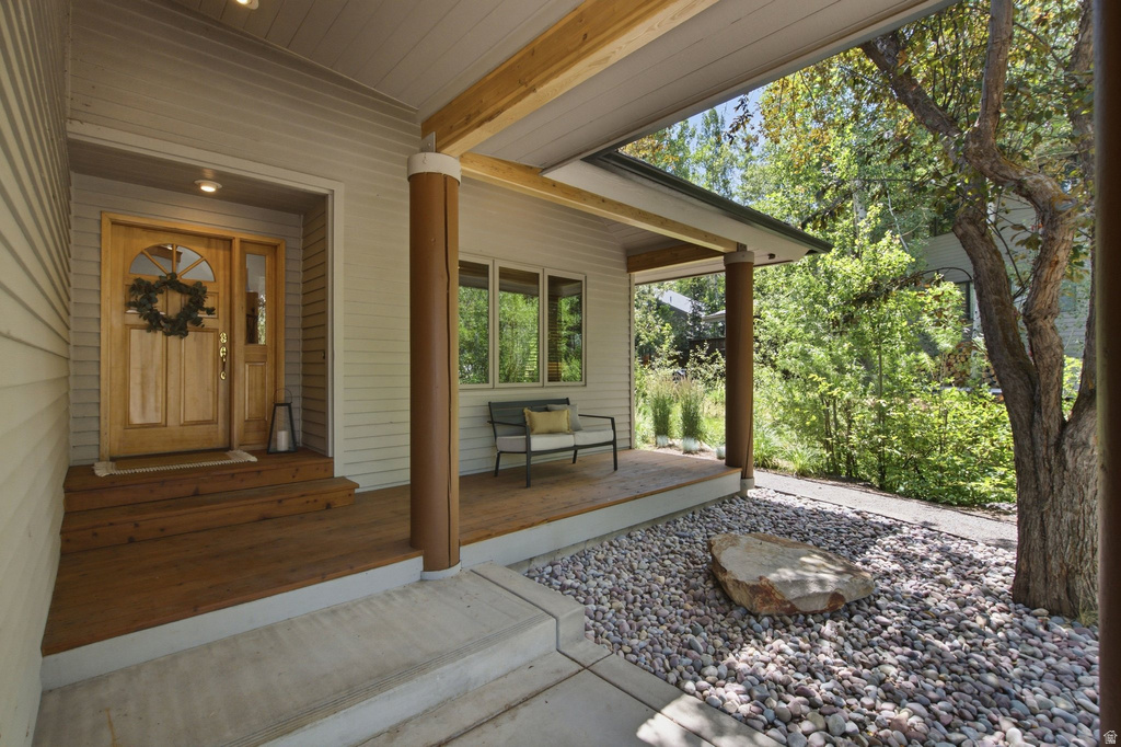 Welcoming covered front porch featuring light wood-finish siding, a natural wood entry door with a decorative glass insert, and supportive columns