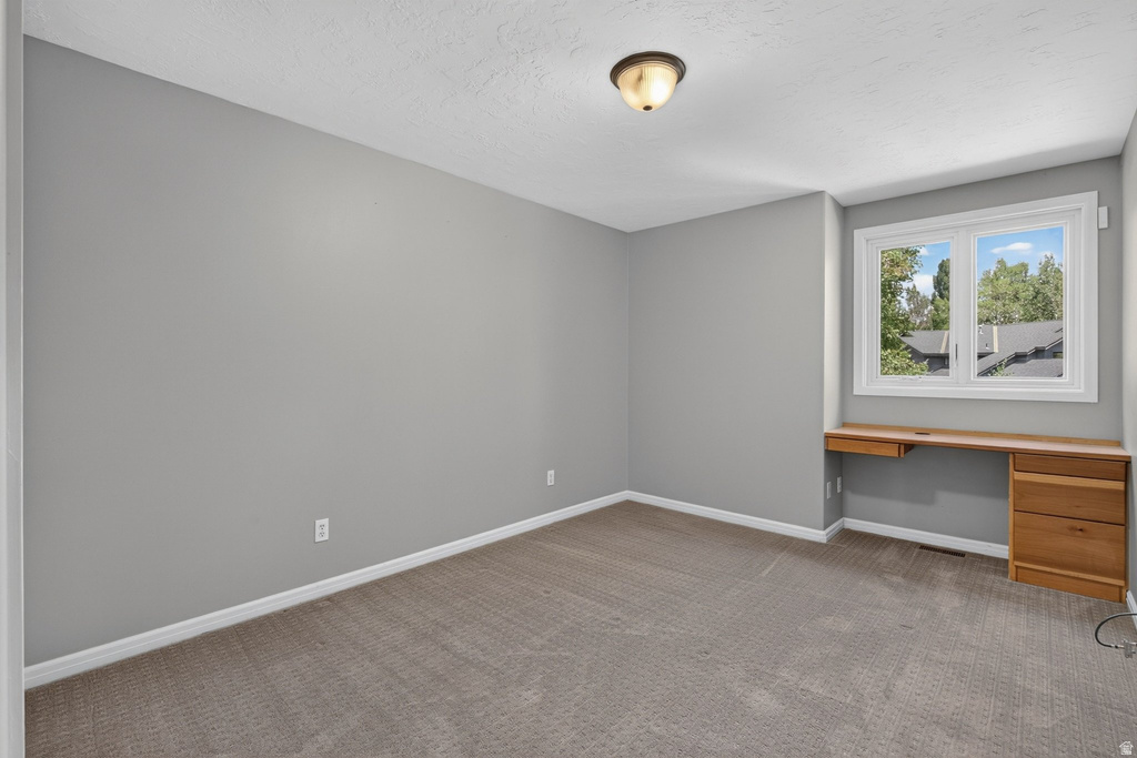 Carpeted room featuring a built-in wooden desk, a window with white trim, and a semi-flush mount ceiling light