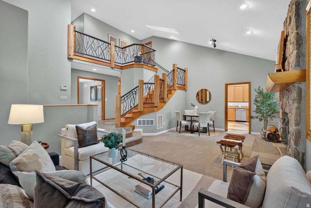 Spacious living area featuring a stone fireplace with a wood mantel, a multi-level wood staircase with metal branch-patterned balusters, and a vaulted ceiling with recessed lighting