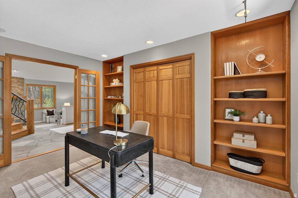 Carpeted room featuring natural wood bi-fold closet doors, built-in shelving, and French doors opening to an adjacent flagstone floor