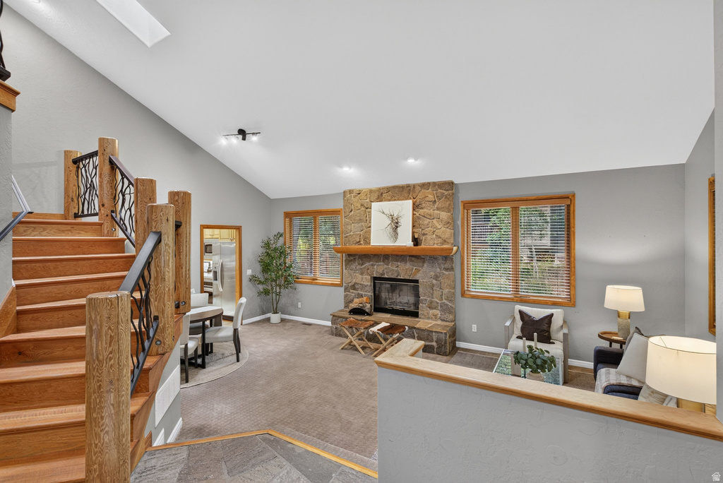 Vaulted ceilings complement an open living space featuring a stone-clad fireplace with a wood mantle