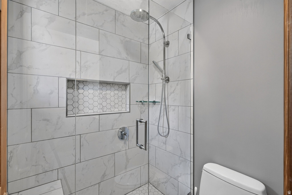 Spacious shower enclosure with floor-to-ceiling tile, a built-in hexagonal tile niche, glass shelving, and a chrome rain shower head with an additional handheld sprayer