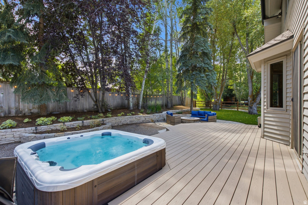 Expansive outdoor deck featuring a hot tub, stone retaining wall, and lush mature trees