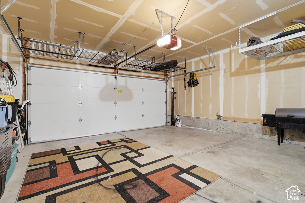 Concrete floor garage featuring a white sectional garage door, multiple overhead storage racks, and an exposed ceiling with an automatic door opener