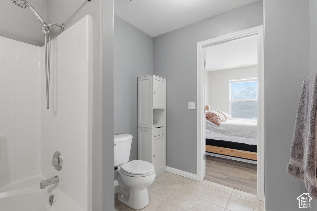 Bathroom featuring a white shower-tub combination with chrome fixtures, a white toilet, and a tall white storage cabinet
