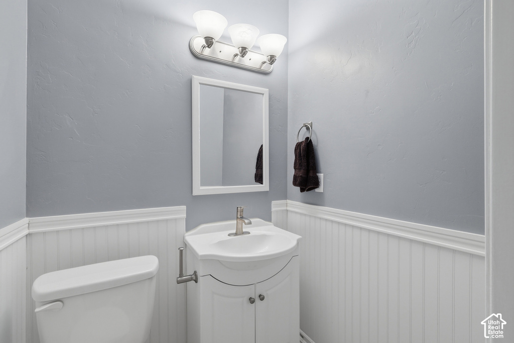 Powder room featuring a white beadboard wainscoting, light gray painted walls, a white framed mirror, and a white vanity with a ceramic basin