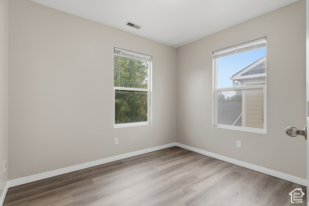 Bright room featuring two windows with horizontal blinds, light neutral wall paint, white trim, and wood-finish flooring