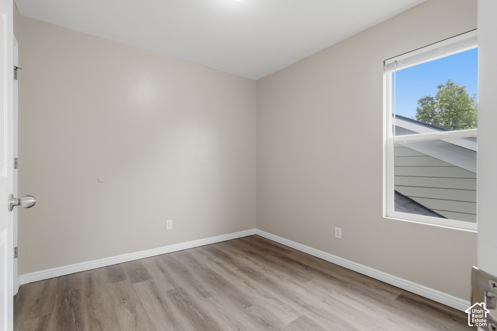 Neutral-toned room featuring wood-finish flooring, white baseboards, and a single window with a white frame