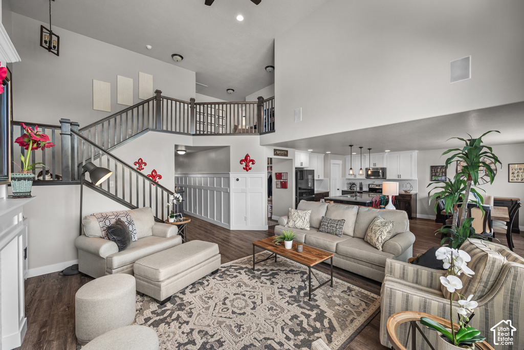 Open-concept living space featuring wood-finish flooring, a two-story ceiling, and a prominent staircase with dark wood railings