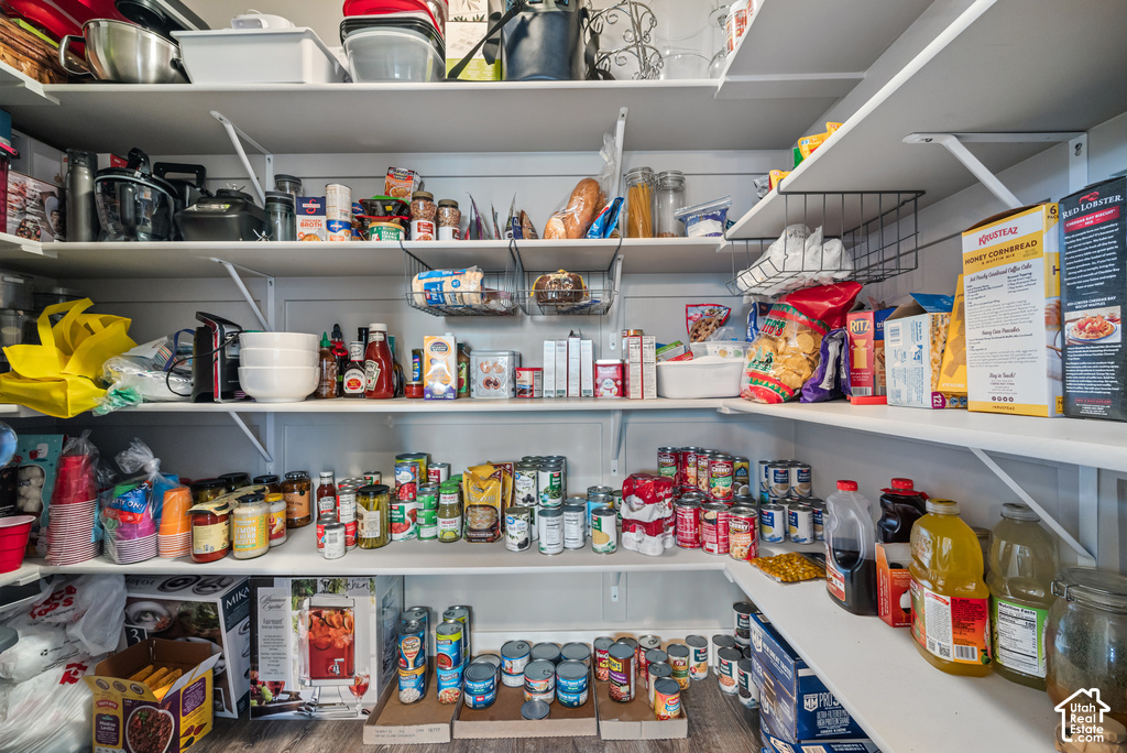 Spacious walk-in pantry featuring extensive white shelving, L-shaped configuration, and wood-finish flooring